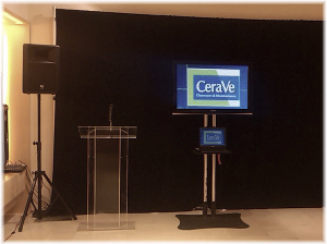 Clear podium with microphone 52'' LED monitor on floor stand with connected laptop on the shelf and PA system setup.